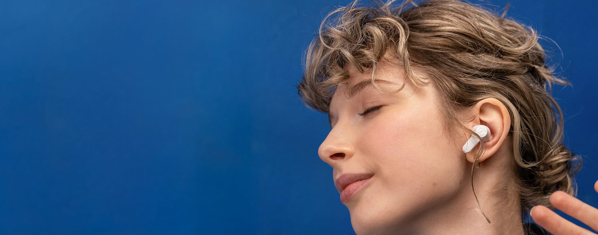 Person mit In-Ear-Kopfhörern bewegt sich zur Musik vor blauem Wand