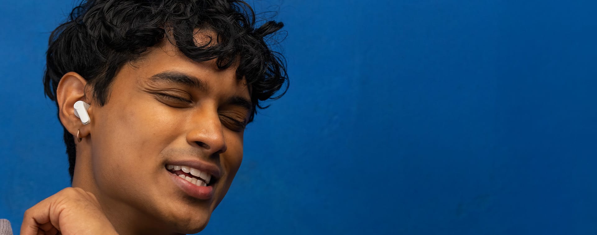 Person mit In-Ear-Kopfhörern bewegt sich zur Musik vor blauem Wand