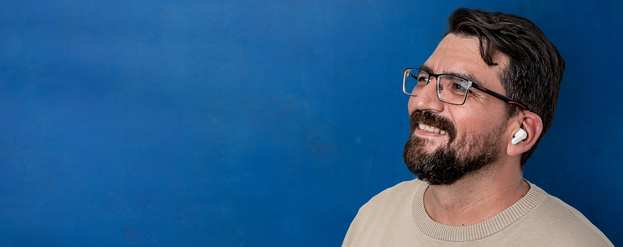 Porträt eines Bankberaters mit In-Ear-Kopfhörern vor blauer Wand